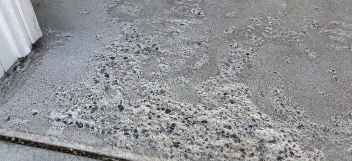 Salt-damaged concrete floor with visible surface wear and exposed aggregate near a garage entry, showing how road salt and winter moisture can deteriorate untreated concrete over time.