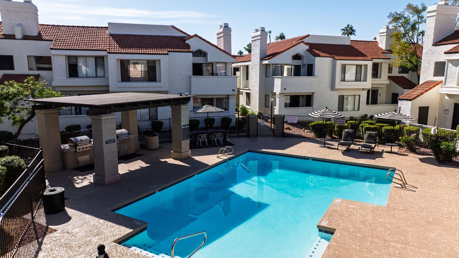 Pool area at an apartment complex; blue pool, white buildings, red tile roofs, sunny day. Talavera Apartments makes pet-friendly apartments in Tempe AZ easy to enjoy.