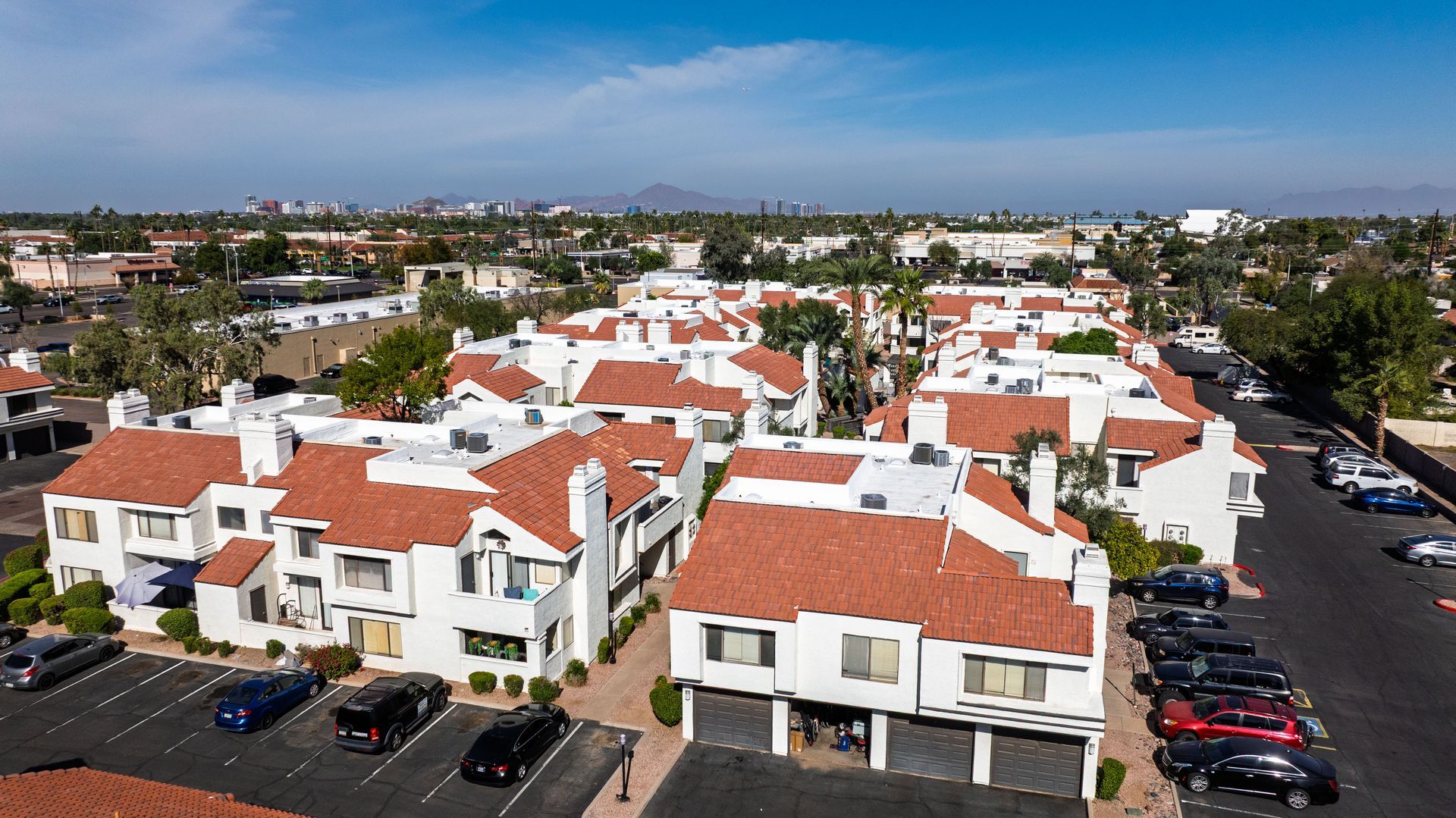 An aerial view of a white multi-unit residential complex with red-tiled roofs and parked cars in Phoenix, Arizona. Talavera Apartments brings modern apartments in Tempe AZ to life—take a look.