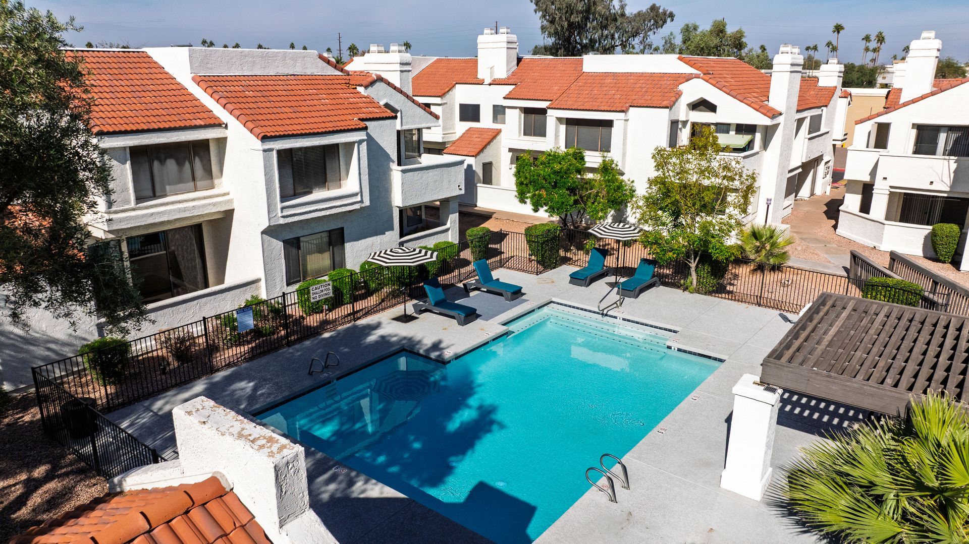 Apartment complex with a pool; white buildings with orange tile roofs; blue lounge chairs. Explore modern living with 1 bedroom apartments in Tempe AZ at Talavera Apartments.