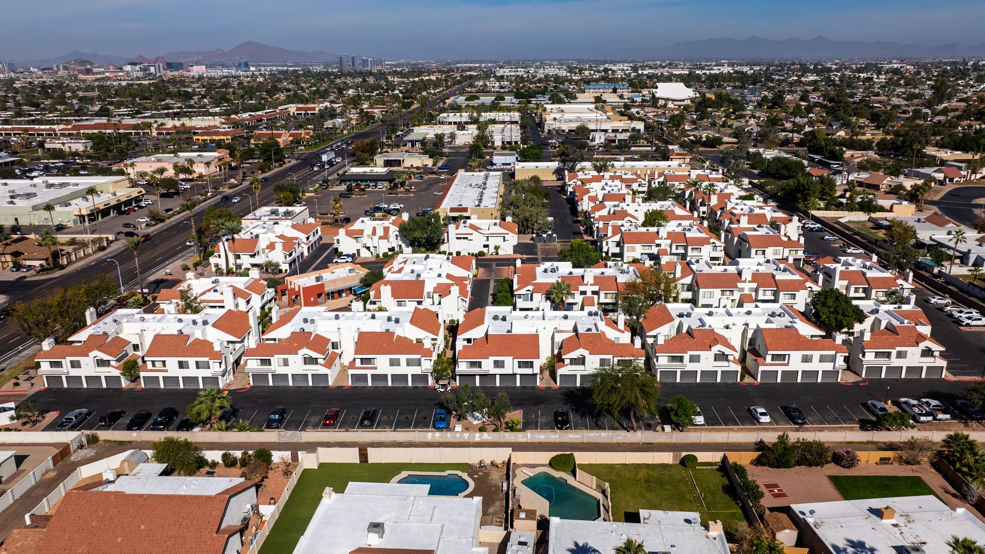 Aerial view of a complex of white buildings with red tile roofs; set in a city with mountains in the distance. Discover efficient 1 bedroom apartments in Tempe AZ at Talavera Apartments.