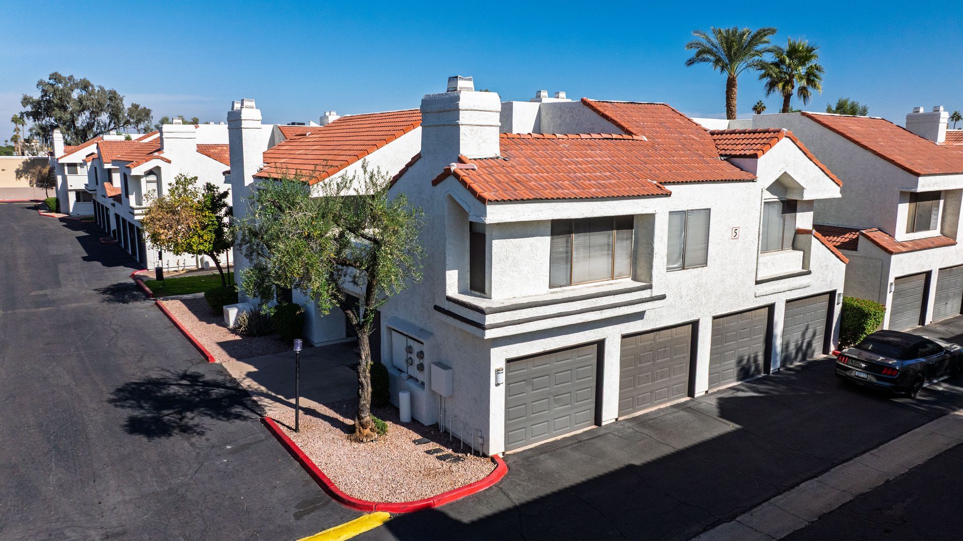 Townhouses with white walls, red tile roofs, and attached garages, under a blue sky. Discover modern Tempe AZ apartment rentals at Talavera Apartments today.