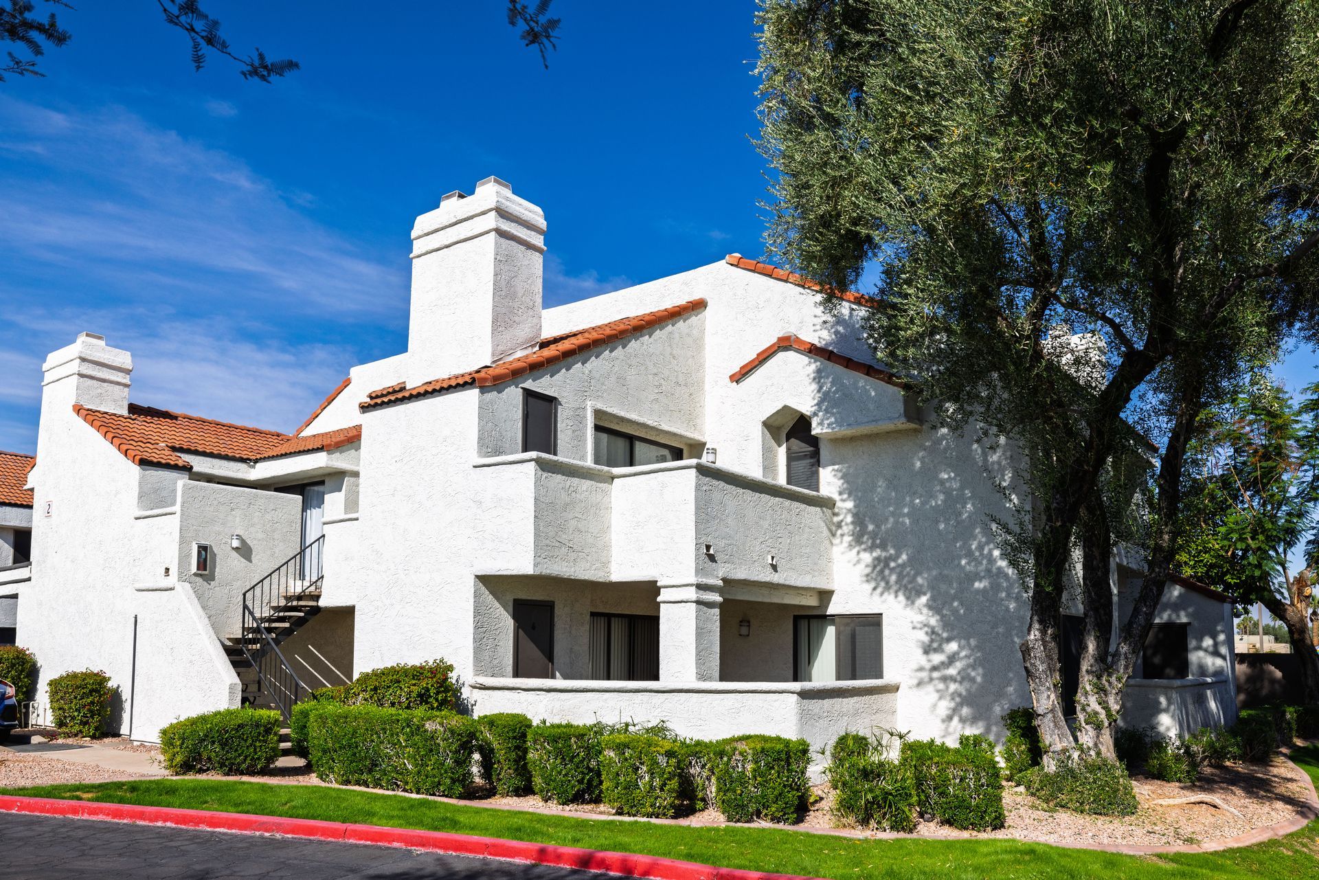 White stucco apartment building with red tile roof, balconies, and a large tree. Talavera Apartments offers thoughtfully planned apartment homes in Tempe AZ.