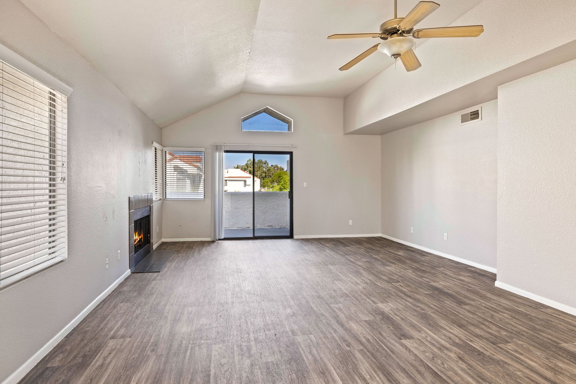 Empty living room with wood-look flooring, fireplace, sliding glass door, vaulted ceiling, and ceiling fan. Talavera Apartments features apartment homes in Tempe AZ—see what’s available.
