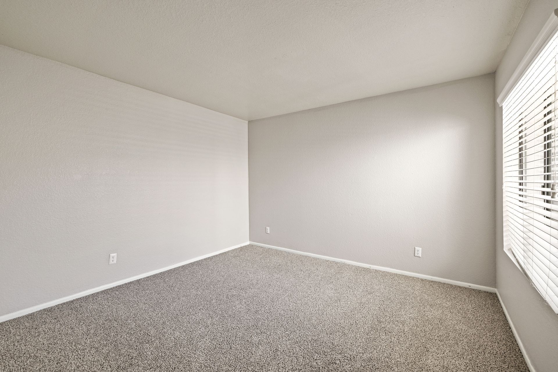 Empty room with gray carpet, off-white walls, and a window with blinds. Explore modern Tempe AZ apartment rentals at Talavera Apartments today.