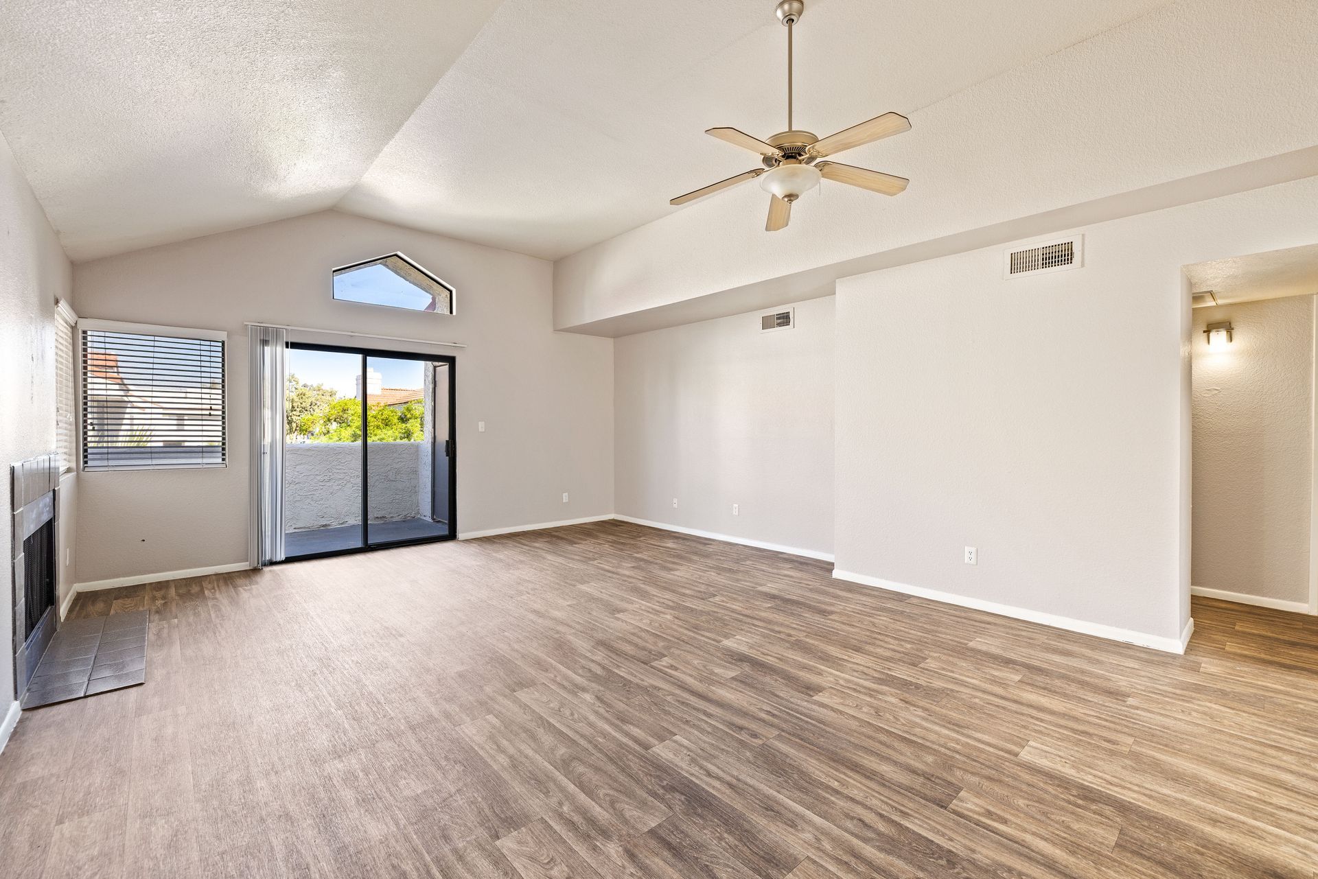 Empty living room with wood-look flooring, vaulted ceiling, sliding door to a balcony, and a fireplace. Talavera Apartments delivers stylish downtown Tempe apartments—explore today.