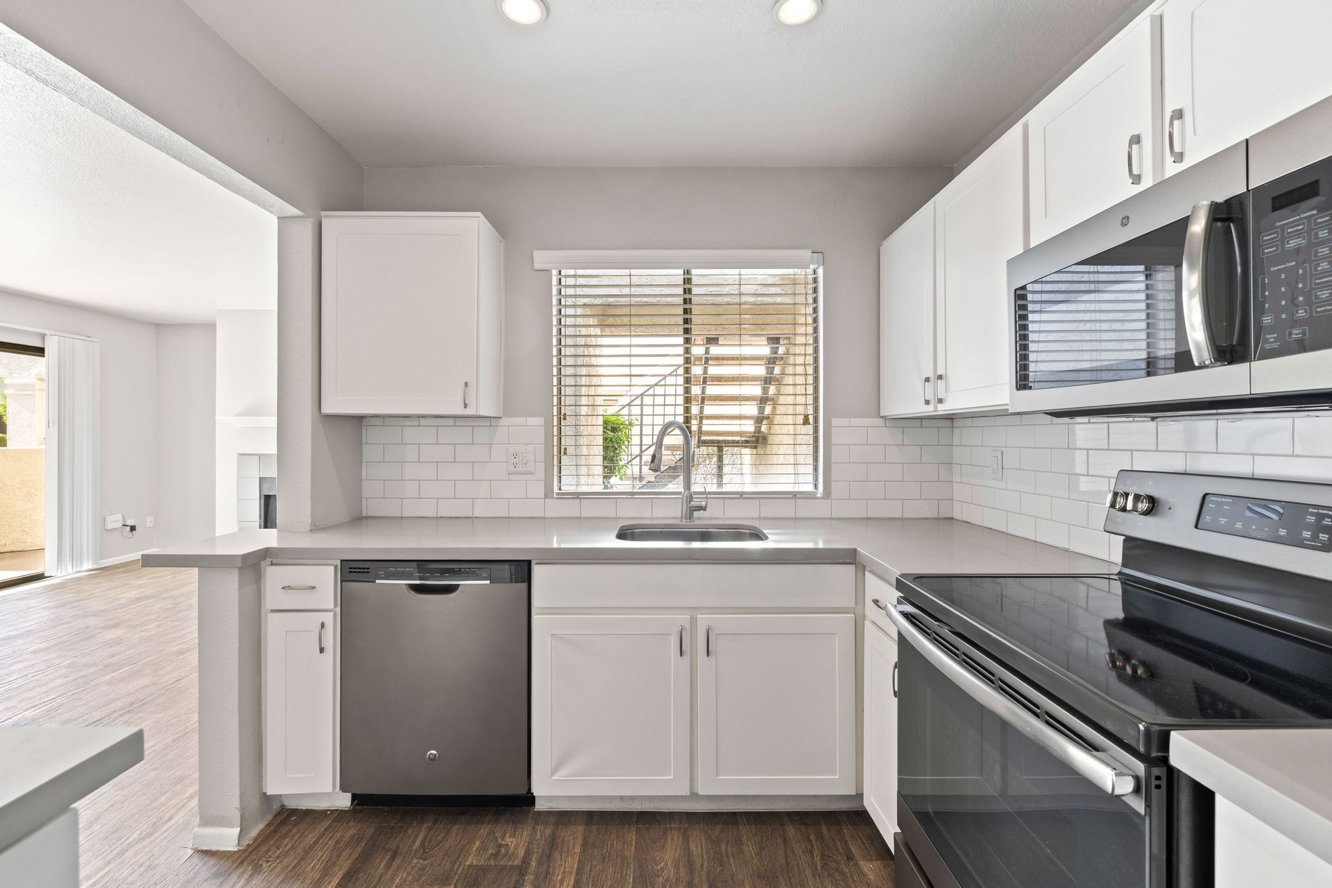 Modern white kitchen with stainless steel appliances, sink, and window overlooking a small patio. Find comfortable Tempe AZ rentals at Talavera Apartments and imagine living here.