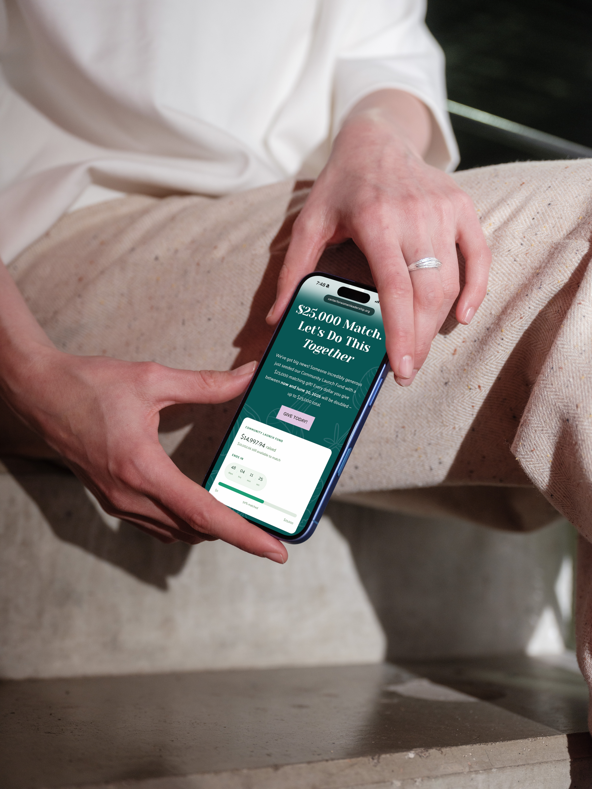 Hands holding a smartphone with a teal screen, resting on beige pants in a seated indoor setting