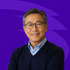 Smiling man in glasses and navy sweater against a purple background