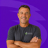 Smiling man with crossed arms in a dark gray shirt against a purple background