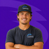 Smiling person in a black cap and T-shirt against a purple background