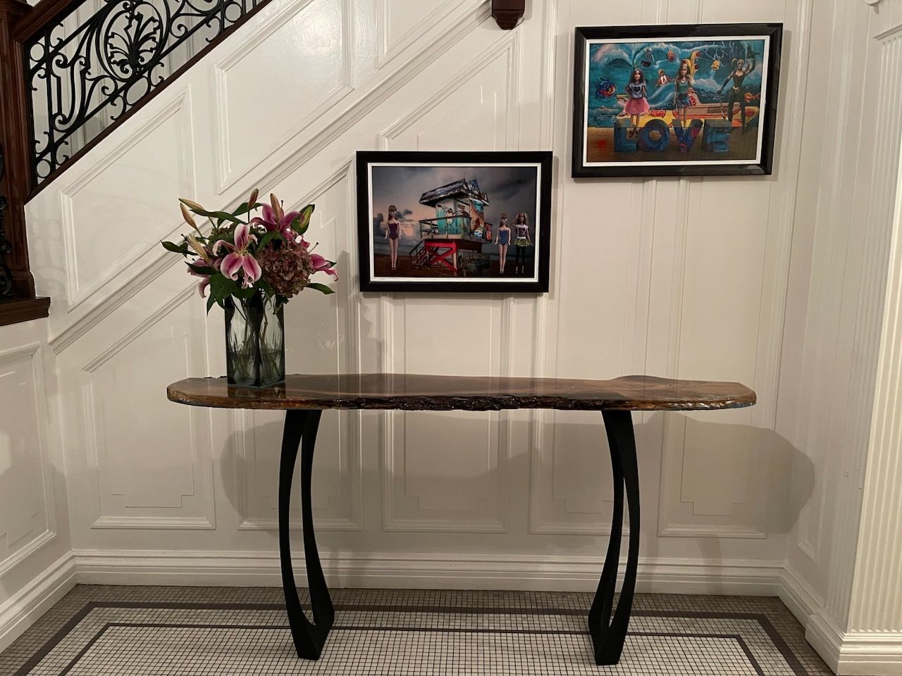 Console table with a flower vase beneath framed art on a staircase wall