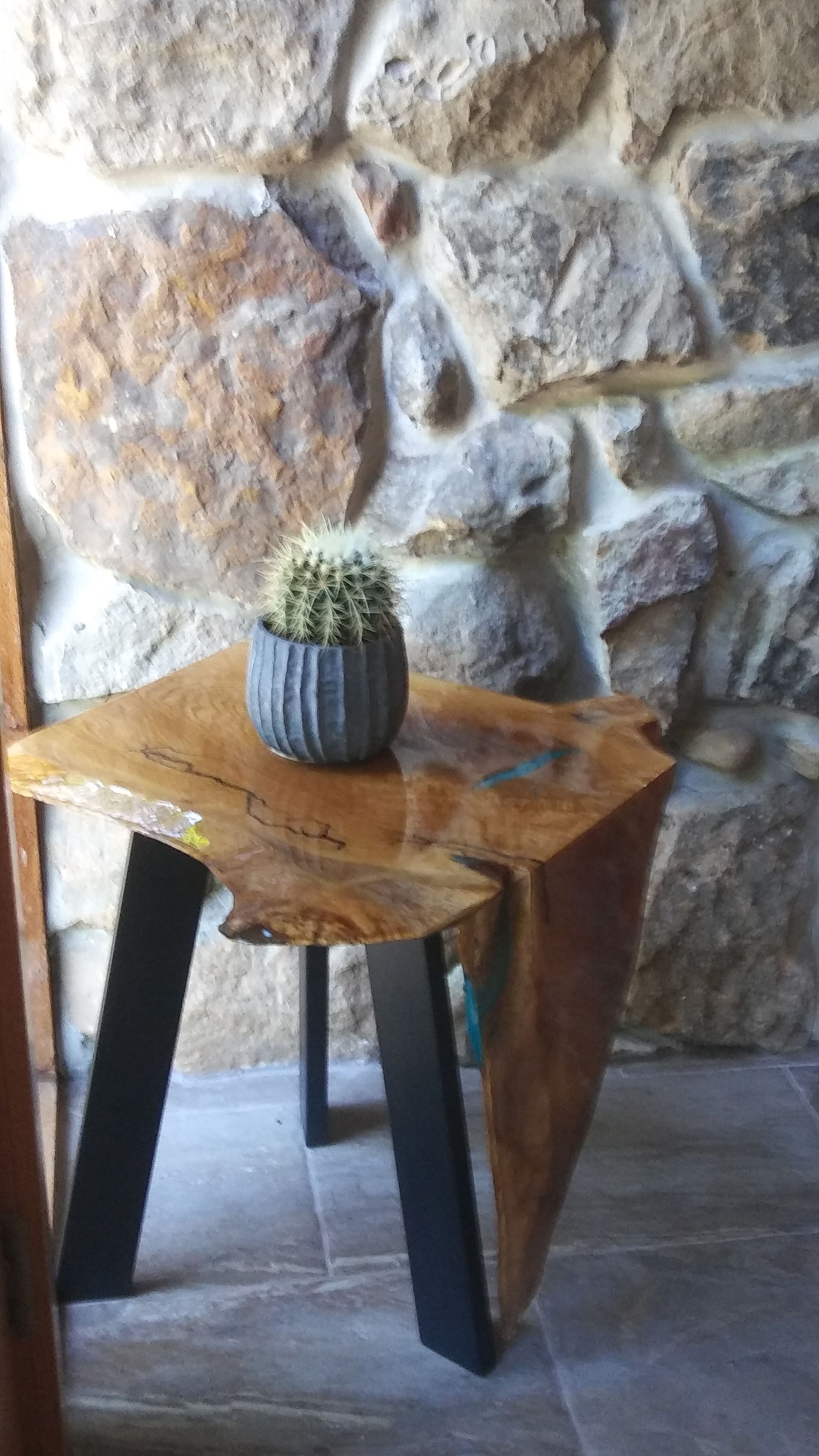 Small cactus on a rustic wooden stool against a stone wall.