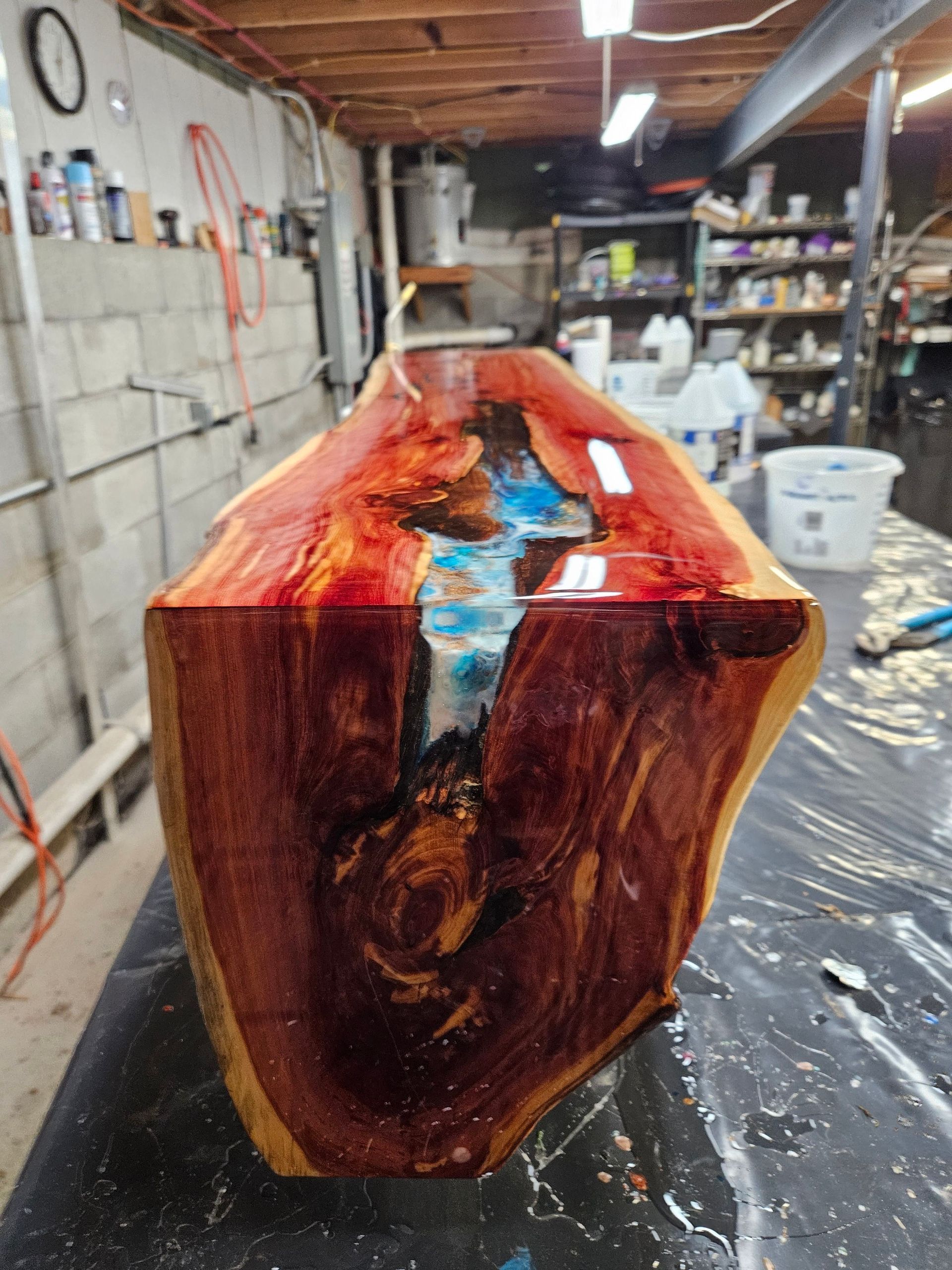 Wooden resin art piece with a glossy red, blue, and amber finish in a workshop.