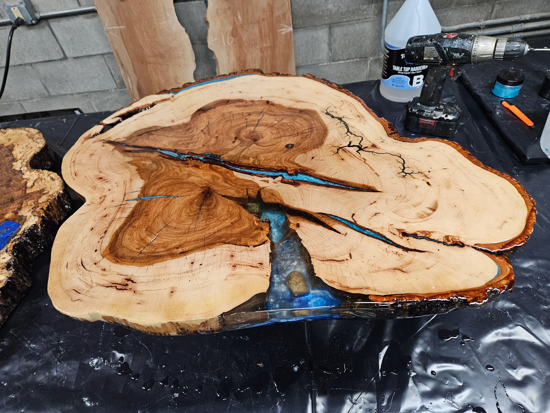Wood slice with blue epoxy crack on a worktable, surrounded by workshop tools and supplies