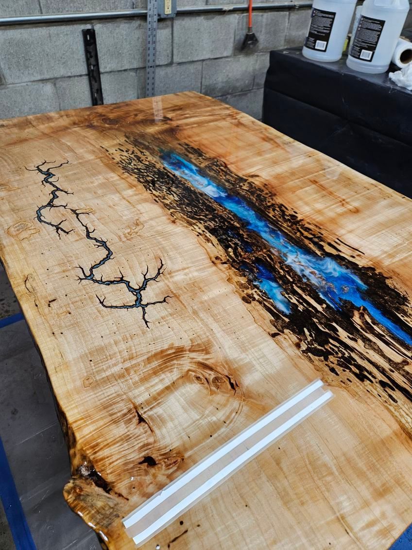 Epoxy-resin wooden tabletop with a blue river design and dark cracks in a workshop.