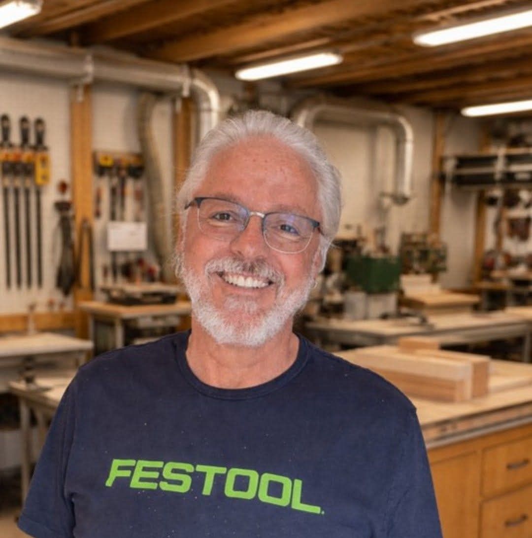 Smiling man in a FESTOOL shirt in a woodworking shop, with tools and wooden workbenches in the background