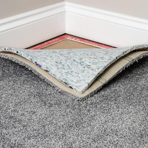 Lifted corner of gray carpet revealing subfloor and tack strip at a wall corner