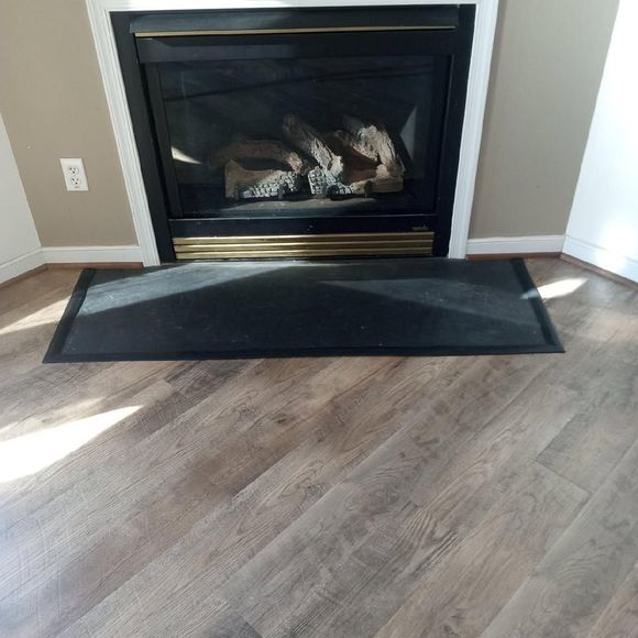 Living room fireplace with black mantel, brass trim, and a dark hearth mat on wood flooring