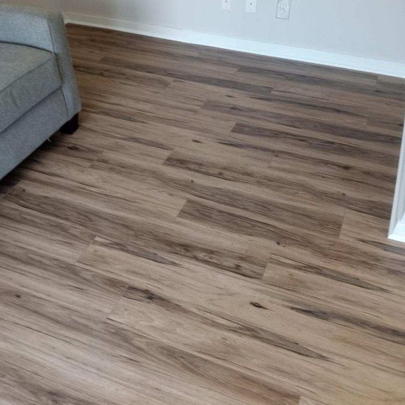 Empty living room with wood-look laminate flooring and a gray sofa corner.