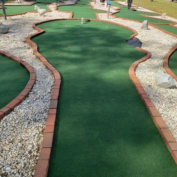 Mini golf course with green turf, curved brick borders, and white gravel paths