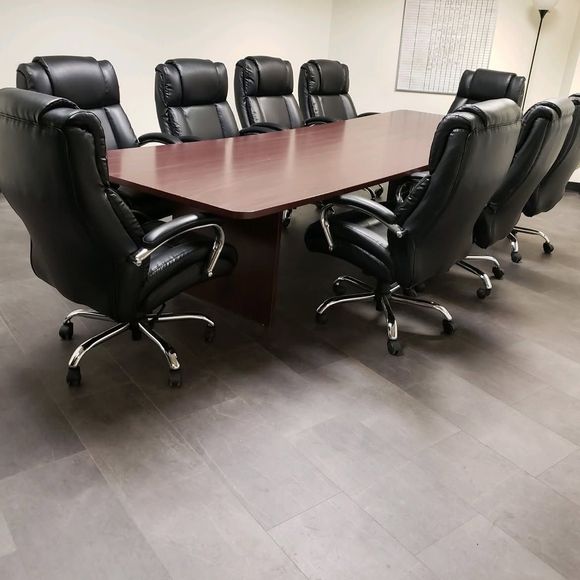 Conference room with a long wooden table surrounded by black leather office chairs.