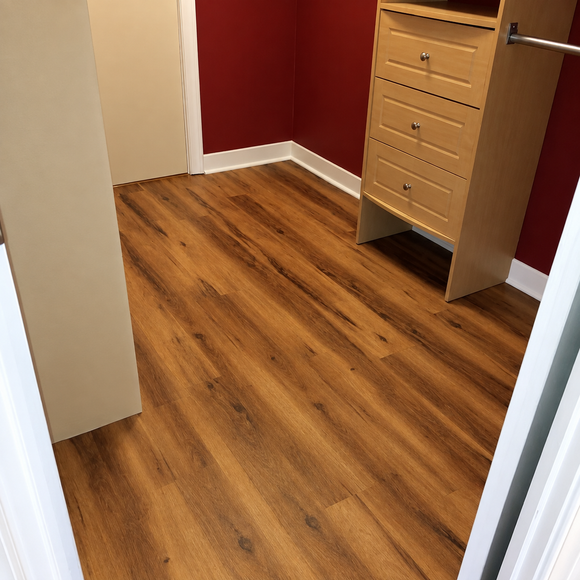 Empty walk-in closet with wood flooring, red walls, white trim, and a wooden dresser.