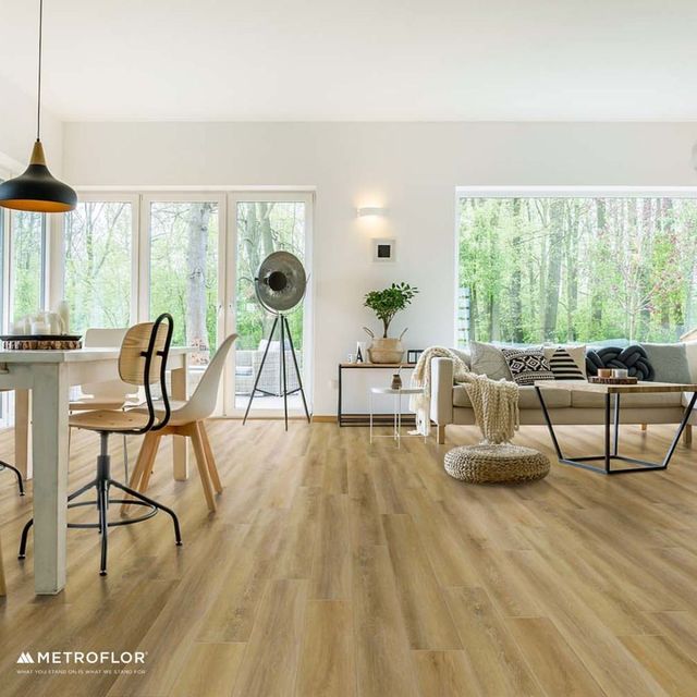 Bright modern living room with large windows, light wood floors, tan sofa, and black lamp and chair accents