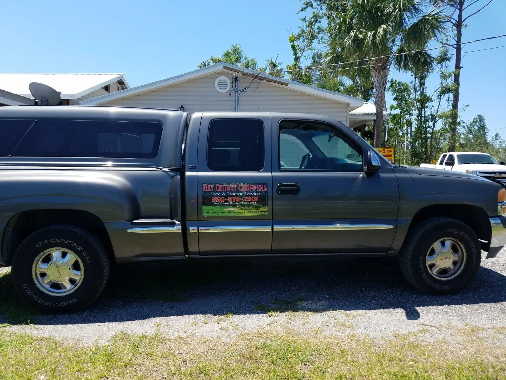 A gray truck with a canopy is parked in front of a house.
