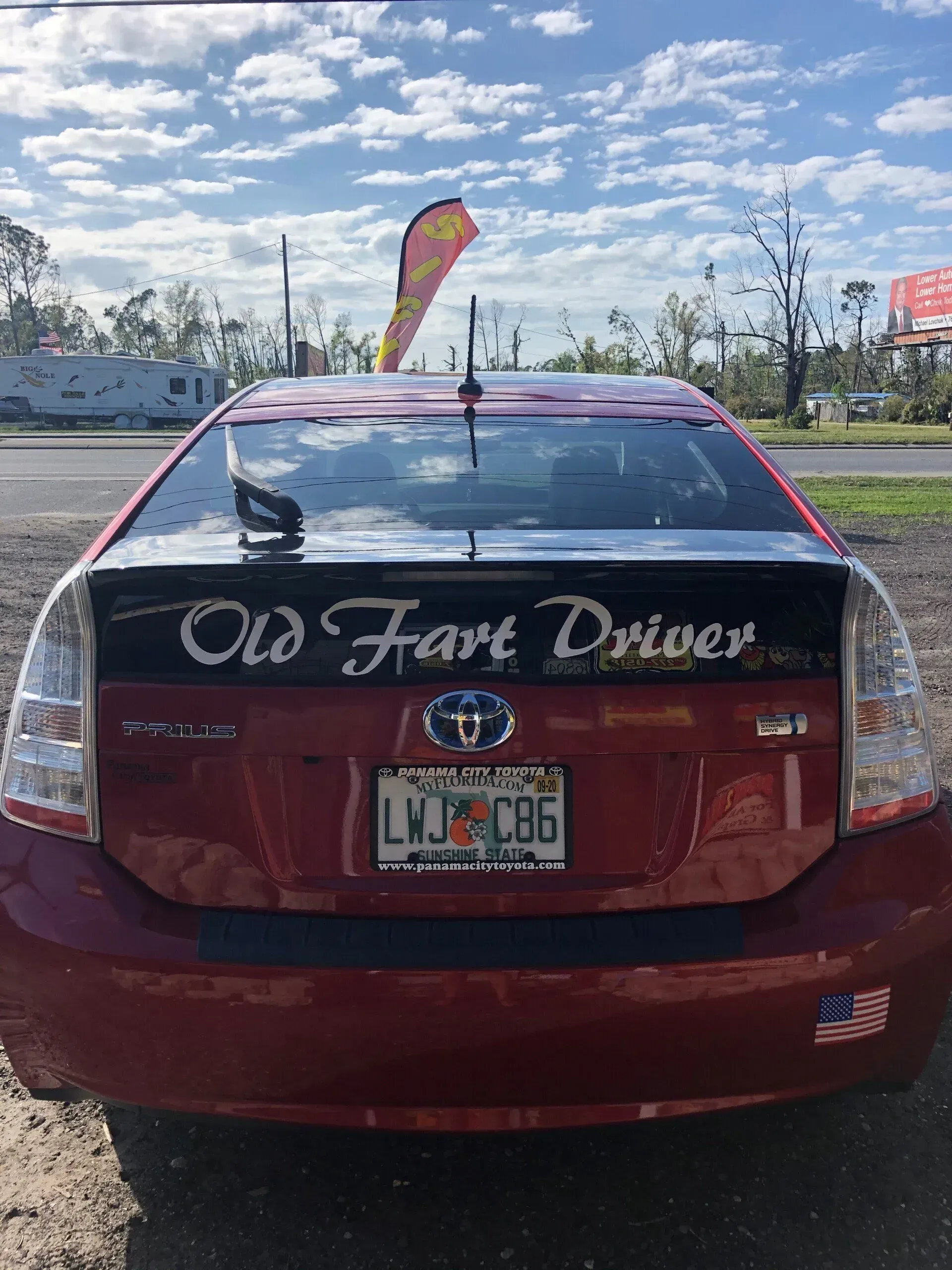 A red car with a bumper sticker that says old fart driver
