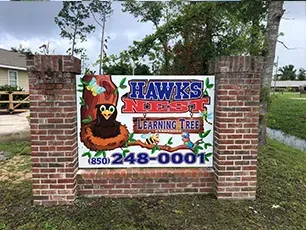 A sign for hawks nest learning tree is on a brick wall