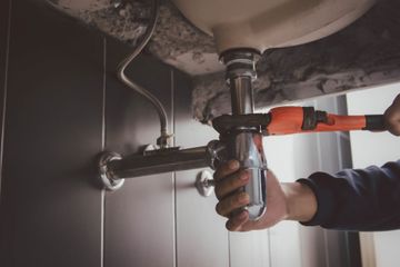 Plumber tightening a sink pipe under a bathroom sink with a wrench