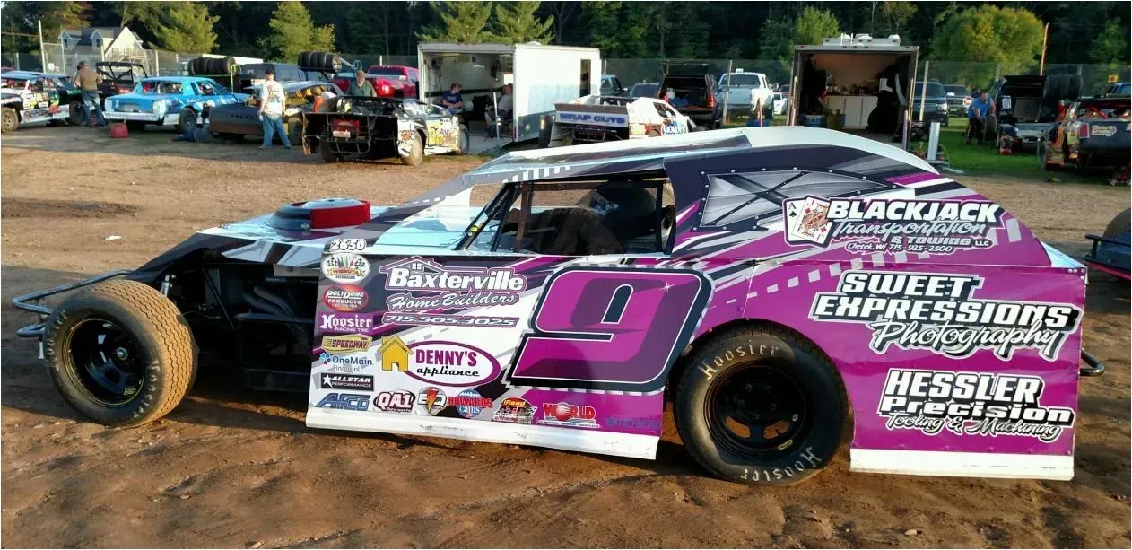 A purple race car is parked in a dirt lot.