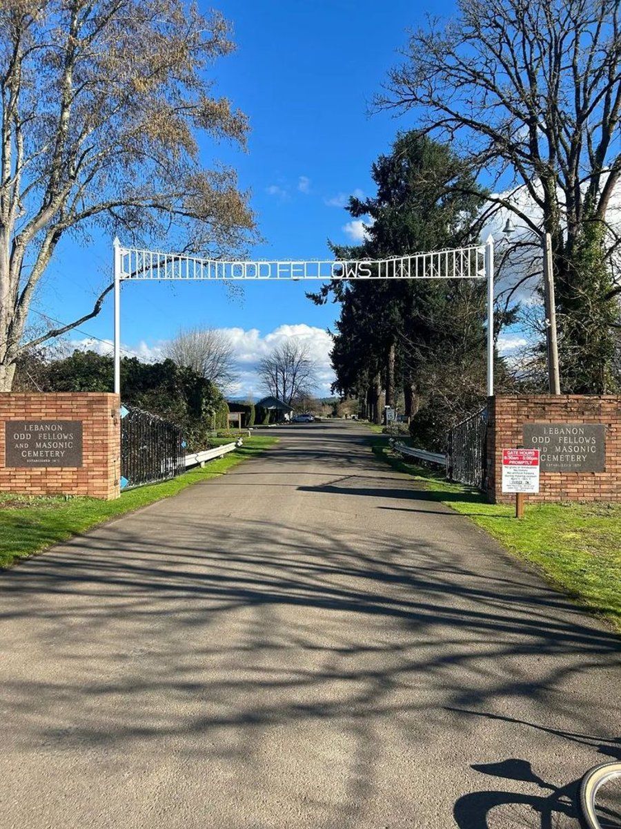 A road with a brick wall and a gate leading to a cemetery.