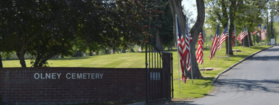 The entrance to olney cemetery is surrounded by trees and flags