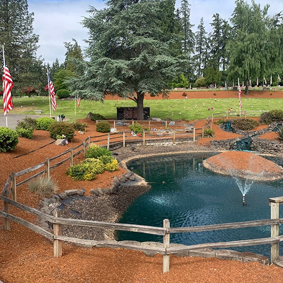 A pond with a fountain in the middle of it surrounded by a wooden fence.