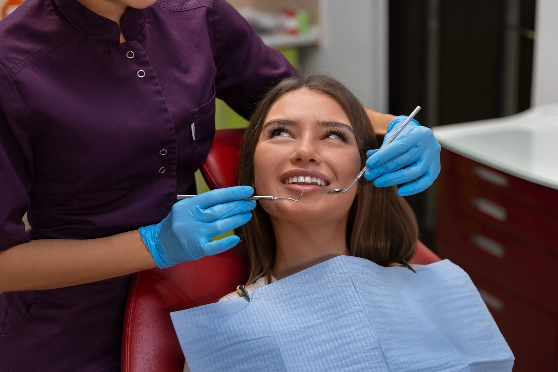 A woman is sitting in a dental chair getting her teeth examined by a dentist.