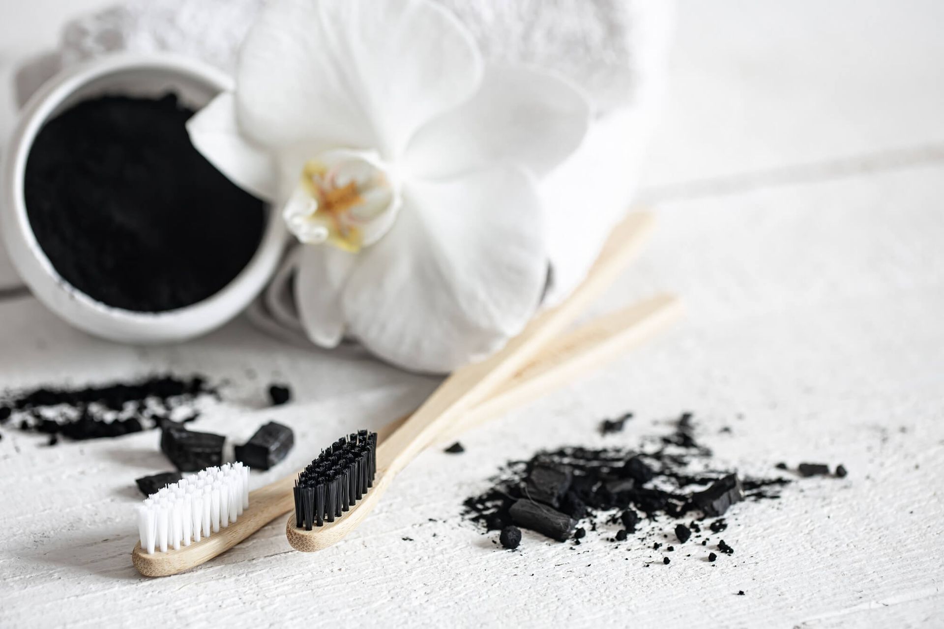 There is a bowl of charcoal next to a toothbrush and a flower.