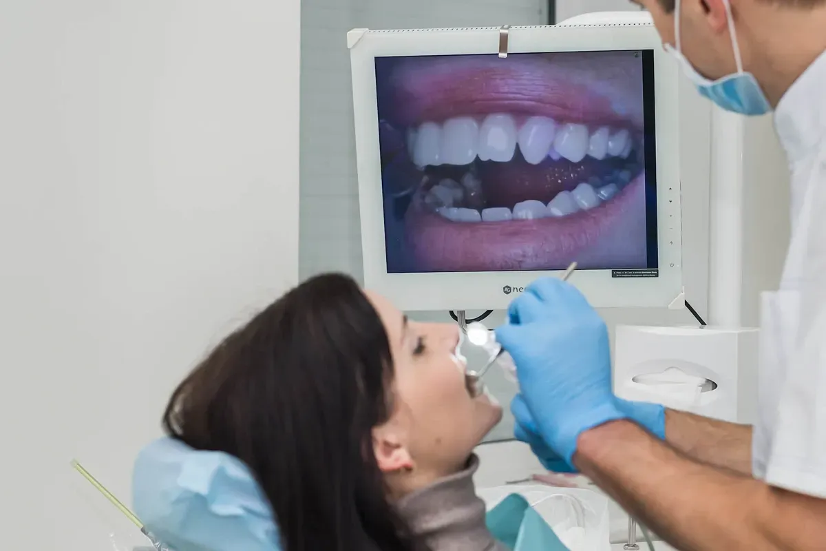 A woman is sitting in a dental chair while a dentist examines her teeth.