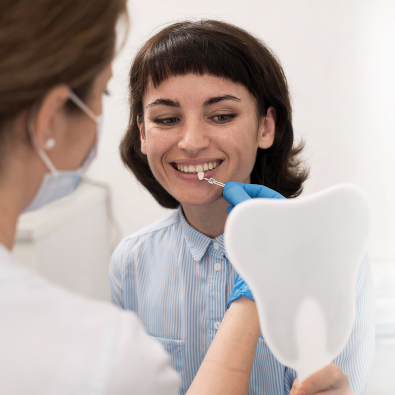 A woman is smiling while looking at her teeth in a mirror.