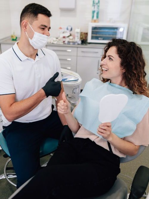 A dentist is giving a thumbs up to a woman in a dental chair.