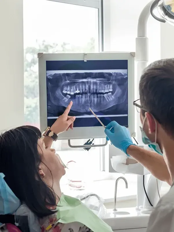 A woman is sitting in a dental chair looking at an x-ray of her teeth.