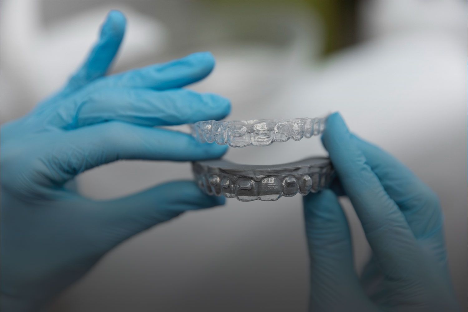 A person wearing blue gloves is holding a clear brace in their hands.