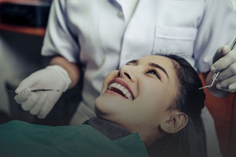 A woman is smiling while having her teeth examined by a dentist.