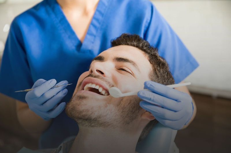 A man is sitting in a dental chair while a dentist examines his teeth.