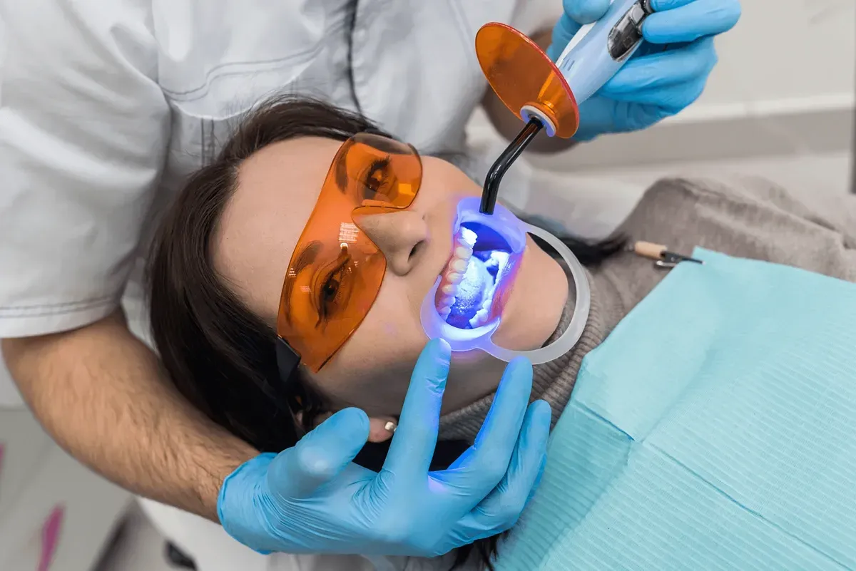 A woman is getting her teeth whitened by a dentist.