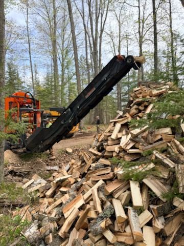 Wood chipper unloading a large pile of split logs in a wooded area