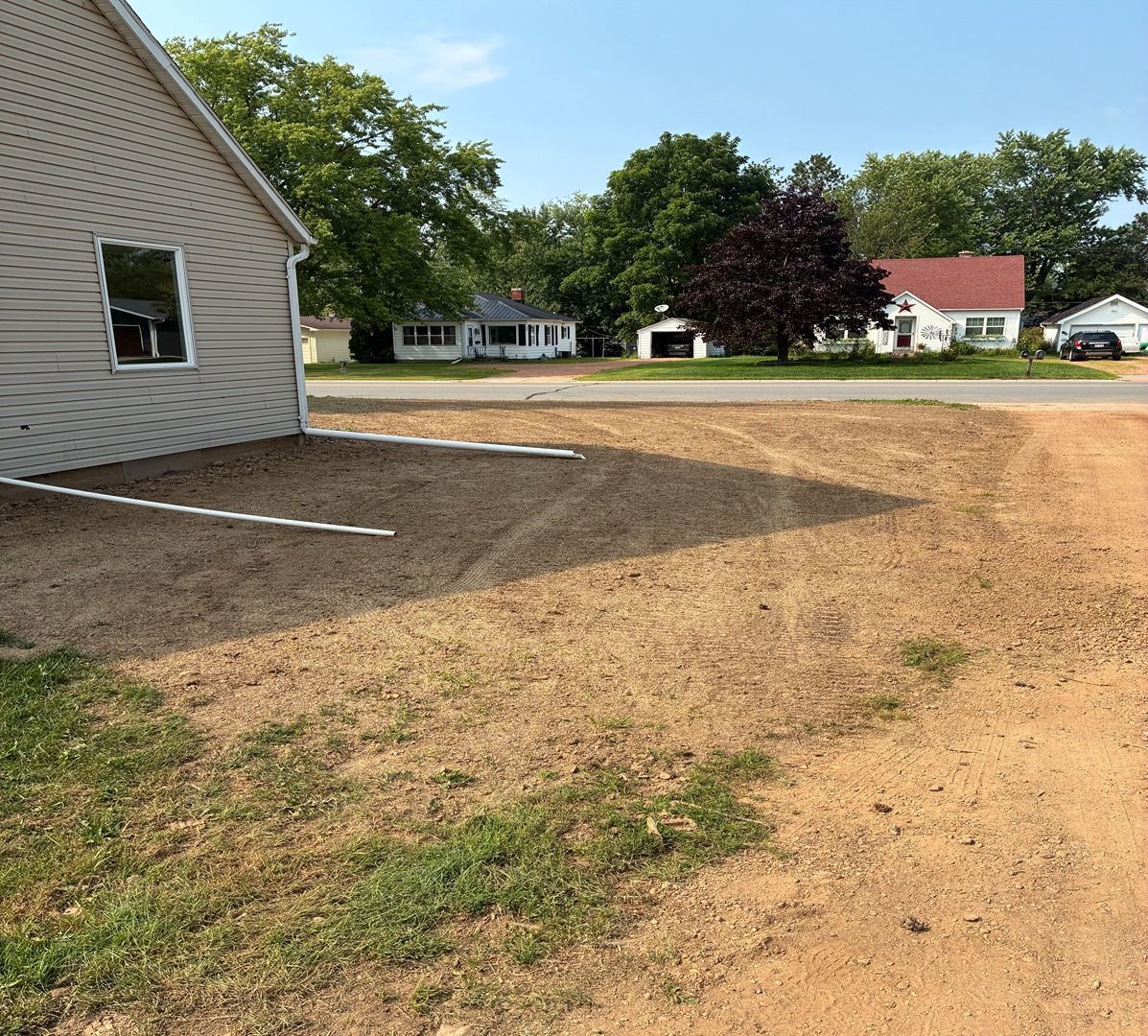 Suburban yard with brown grass beside a house, street, and trees in the background