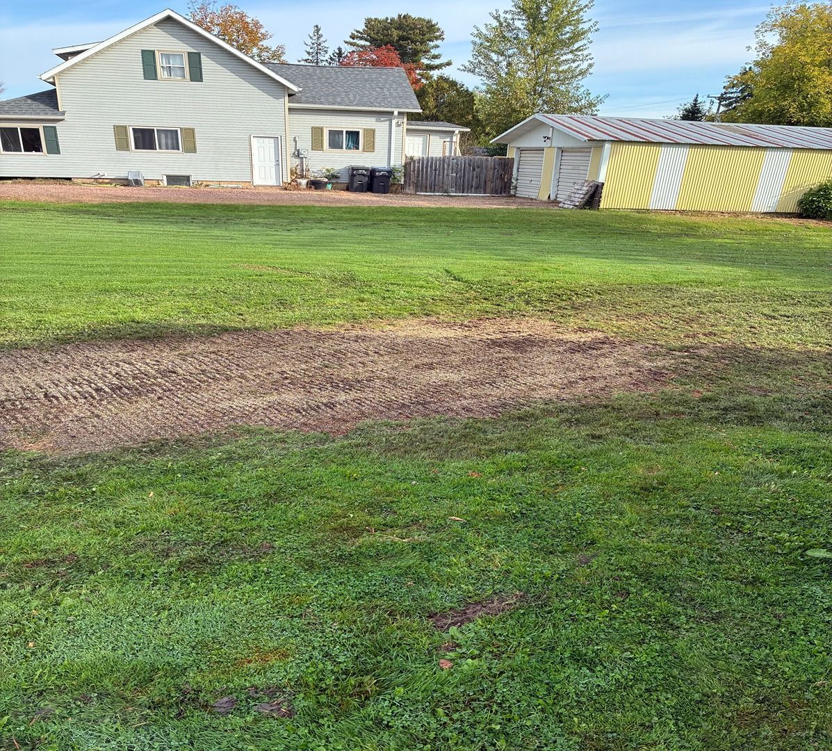 Grassy backyard with a brown bare patch, white house, and yellow-white striped shed in the background