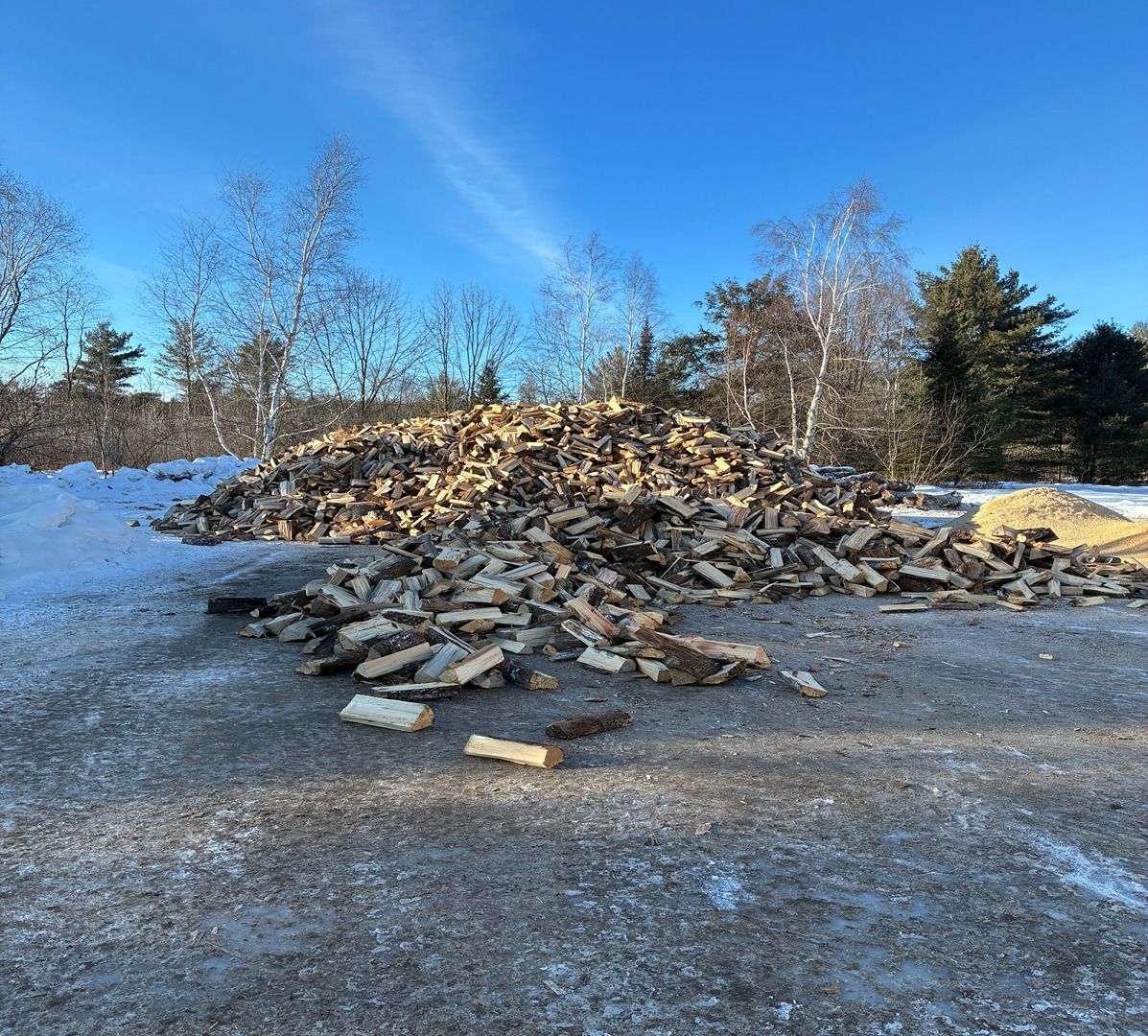 Pile of cut logs on a snowy roadside under a blue sky